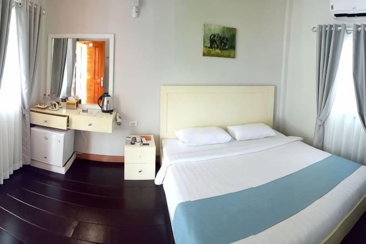 A hotel room with a bed, a dresser, a mirror, a nightstand, and a painting on the wall.