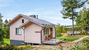 A pink wooden cabin with a porch and a small deck, surrounded by greenery and trees. - Villa ebba by Interhome (Sysmä)