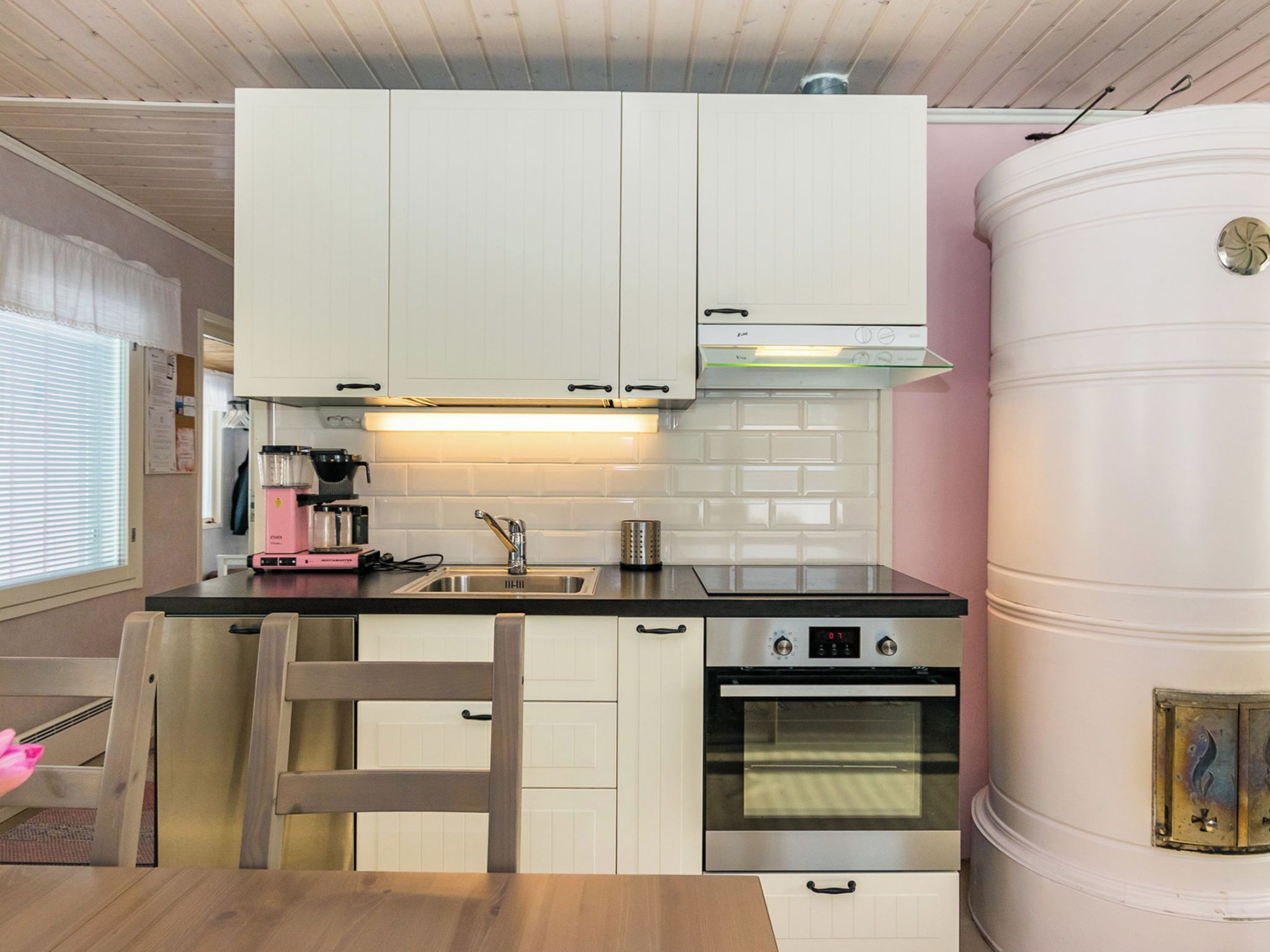 Een compacte keuken met witte kastjes, een roestvrijstalen fornuis en een grote boiler.