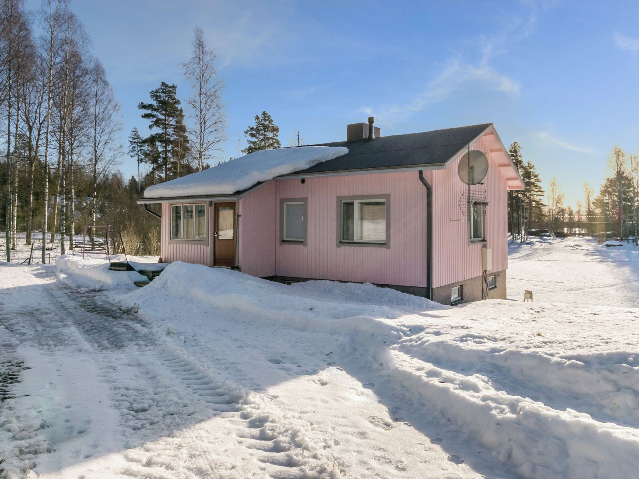 A pink house with a snow-covered roof and a driveway leading to it.