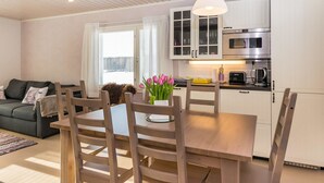 A modern kitchen with white cabinets, a stainless steel oven, and a dining area with wooden chairs and a table. - Villa ebba by Interhome (Sysmä)