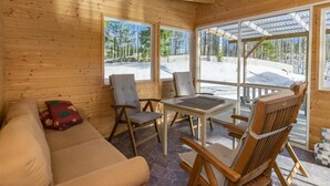 A cozy wooden cabin with a stone floor, a sofa, two chairs, a table, and large windows offering a view of a snowy landscape. - Villa ebba by Interhome (Sysmä)