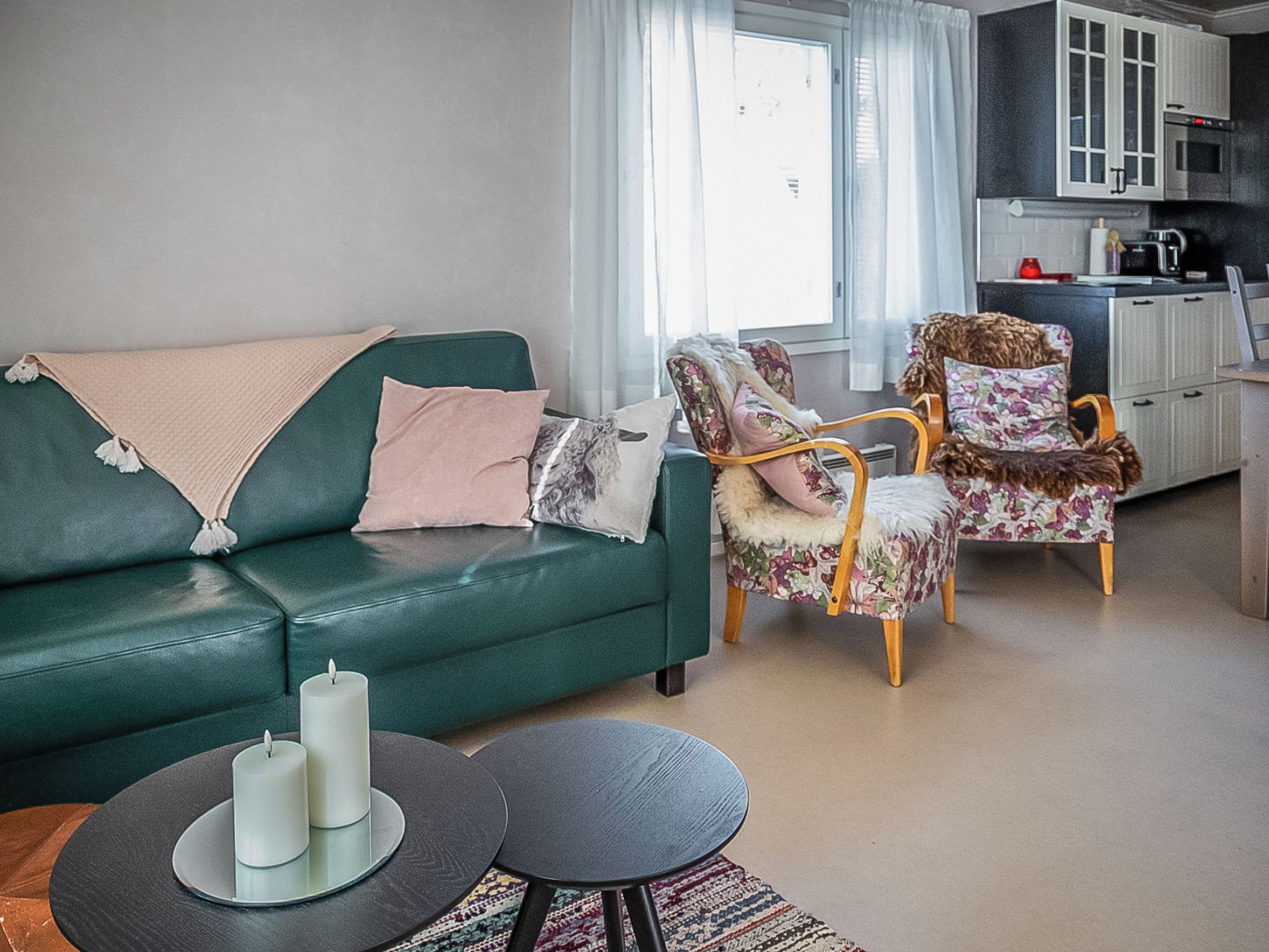 A living room with a green sofa, two armchairs, a coffee table, and a kitchen area in the background.