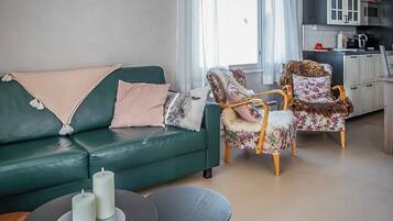 A living room with a green sofa, two armchairs, a coffee table, and a kitchen area in the background.
