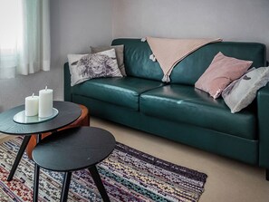 En grøn lædersofa med et mønstret tæppe, et rundt sofabord med stearinlys og en vævet måtte.