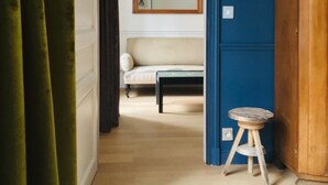 Una habitación con un armario de madera, un taburete pequeño, un sofá y un espejo en la pared.