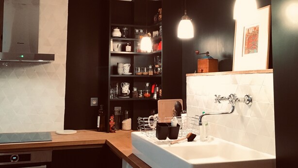 Una cocina moderna con armarios oscuros, encimera blanca y horno empotrado. Hay un lavamanos con grifo y un espejo encima.