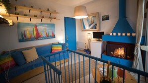 Un soggiorno con un divano blu, un quadro con barche a vela, un caminetto con candele e una ventola a soffitto.