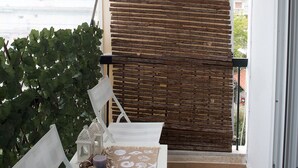 Un balcone con parete in legno a lamelle, un tavolo bianco con candela e oggetti decorativi, e una sedia.