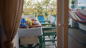 Un'area pranzo all'aperto con un tavolo apparecchiato per due, sedie, un'amaca e piante in vaso.
