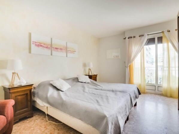 Une chambre à coucher avec un lit, deux tables de chevet, une lampe et une fenêtre avec des rideaux.