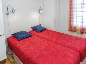 A room with two beds, each with a red bedspread and a blue pillow. There are wall-mounted lamps on either side of the beds. - Nelikko a by Interhome (Kuusamo)