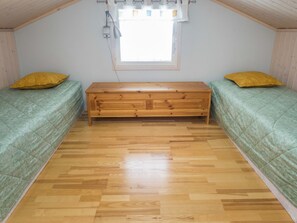 Ein kleines Zimmer mit zwei Betten, einer hölzernen Bank und einem Fenster.