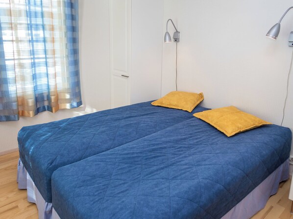 Ein Schlafzimmer mit einem Bett, zwei Kissen, einem Nachttisch, einer Lampe und einem Fenster mit Vorhängen.