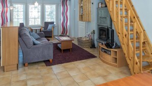A cozy living room with a sofa, armchair, and a fireplace. There's a wooden staircase leading to an upper level. - Nelikko a by Interhome (Kuusamo)