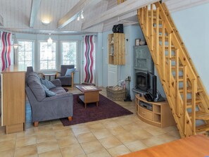 A cozy living room with a fireplace, a sofa, a coffee table, and a wooden staircase. - Nelikko a by Interhome (Kuusamo)