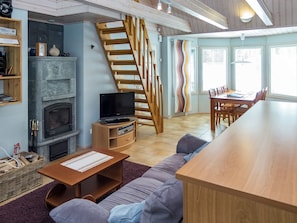 Ein modernes Wohnzimmer mit Kamin, einer Holztreppe und einem Essbereich mit großem Tisch und Stühlen.