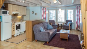 A cozy living area with a sofa, chairs, a small table, and a kitchen with a stove, oven, and microwave. - Nelikko a by Interhome (Kuusamo)