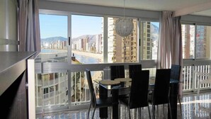 Un balcon avec un coin repas, de grandes fenêtres offrant une vue sur la ville et un luminaire suspendu.