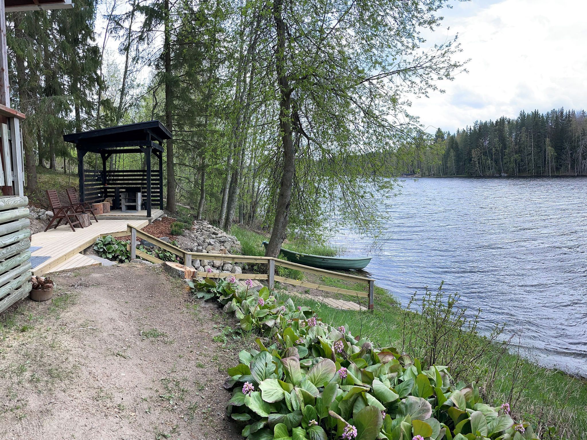 Järven rannalla sijaitseva mökki, jossa on puinen terassi, katettu oleskelualue ja laituriin kiinnitetty vene.