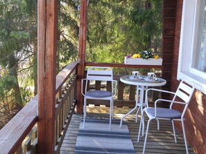 A wooden deck with a table and two chairs, a window, and a railing.