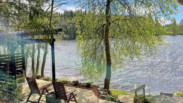A wooden deck with two chairs and a table overlooking a calm lake, surrounded by trees and a wooden structure. - Hellinki by Interhome (Virrat)