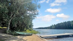 A sandy beach with a dock extending into a calm lake, surrounded by dense trees. - Hellinki by Interhome (Virrat)