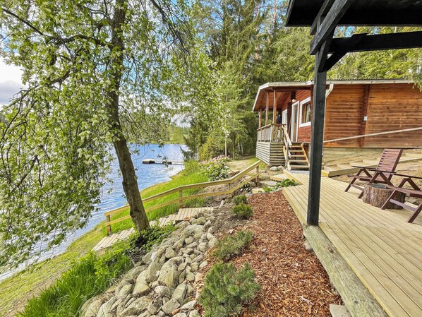 A wooden deck with a stone pathway leading to a cabin by a lake.