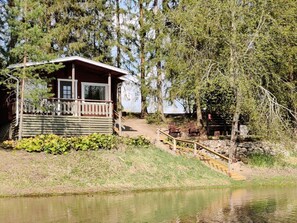 A cabin with a porch, a small deck, and a pond in front.