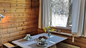 A wooden cabin interior with a dining table set for two, a vase with yellow flowers, and a window with a view of trees. - Hellinki by Interhome (Virrat)