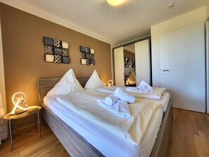 Et hotelværelse med en stor seng, to sengeborde, en stol, et spejl og dekorativ vægkunst.