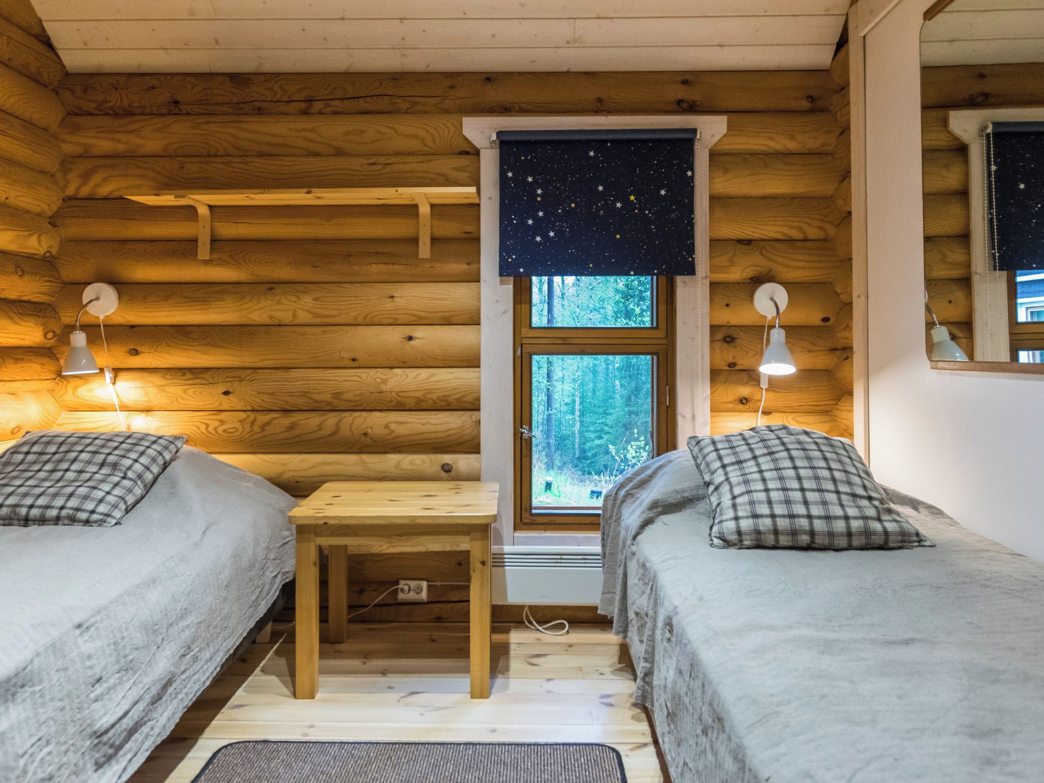 Uma cabana com duas camas, uma mesinha e uma janela com vista para uma noite estrelada.