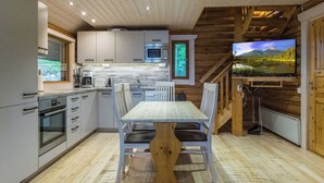Eine moderne Küche mit Holzakzenten, einem Essbereich und einem an einer Holzwand montierten Fernseher.