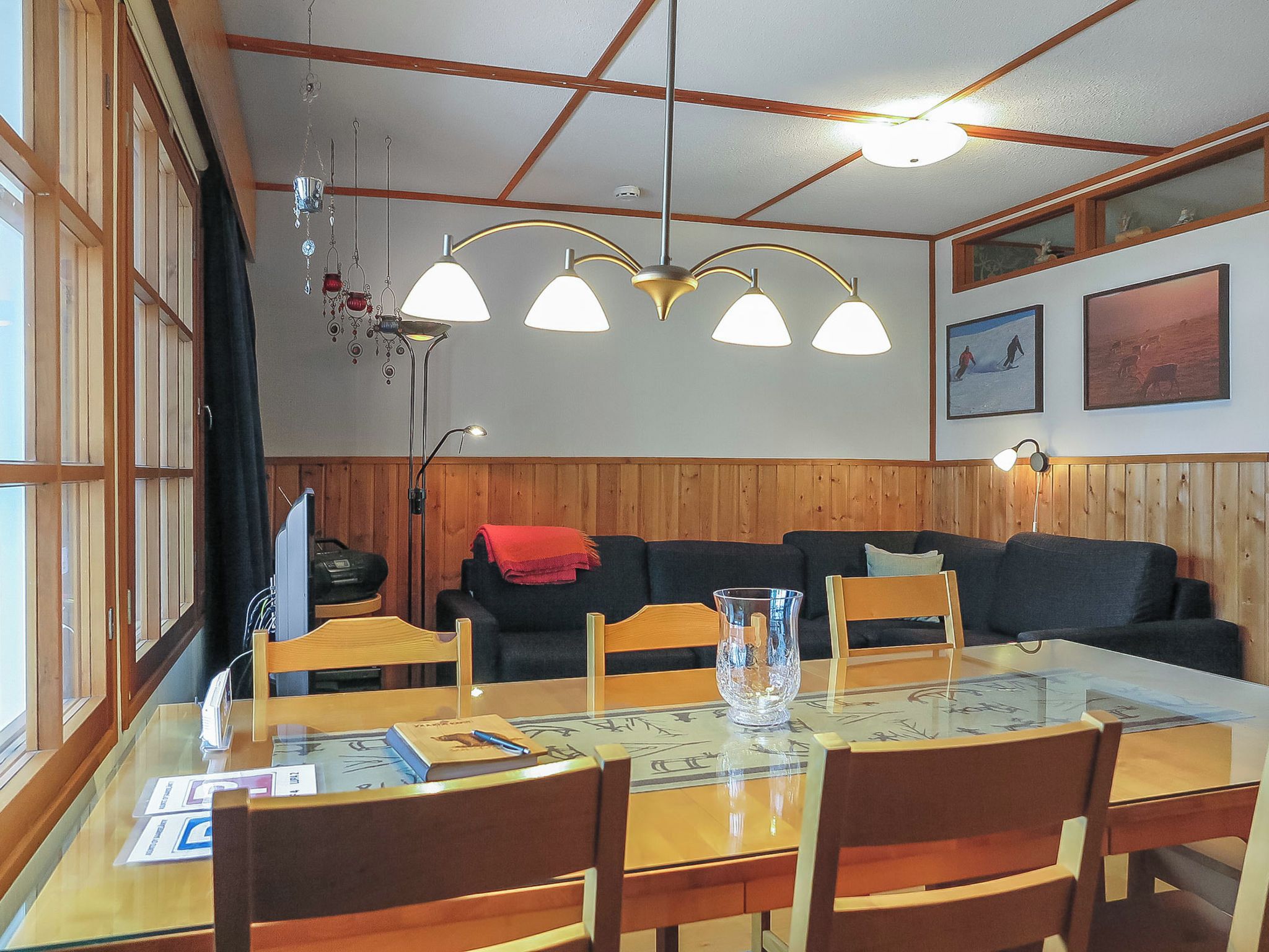 Een eetgedeelte met een glazen tafel, houten stoelen, een zwarte bank en een plafondlamp.