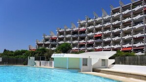 Een zwembad naast een meerhoog hotel met balkons.