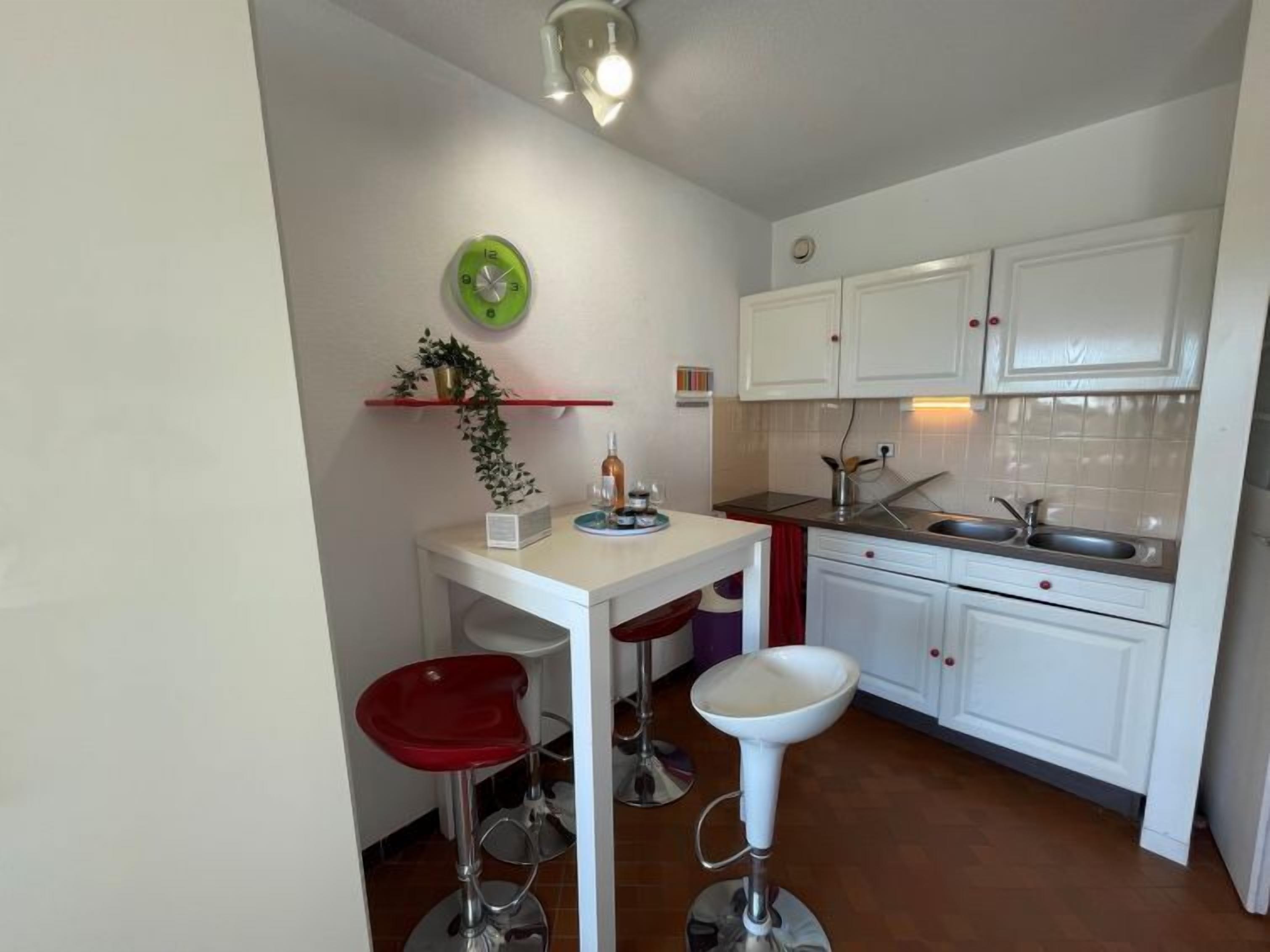 Une cuisine compacte avec des meubles blancs, un évier, un plan de travail et un petit coin repas équipé de deux tabourets.
