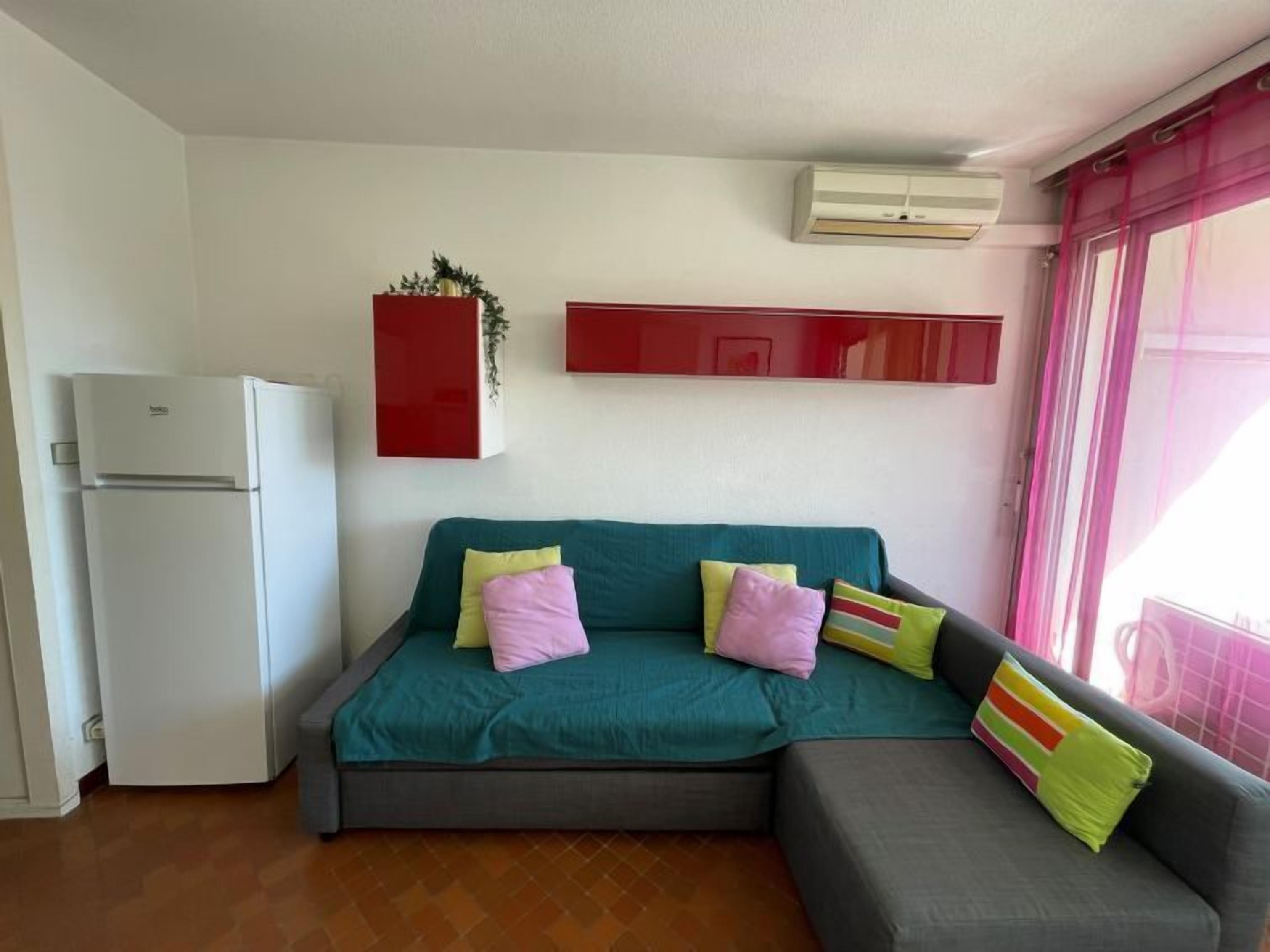 A compact living space with a sofa, a small refrigerator, and a wall-mounted air conditioner.