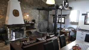 Une cuisine rustique aux murs de pierre, dotée d’un poêle à bois et d’un coin repas avec des sièges en cuir.