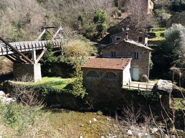 A stone building with a tiled roof, a bridge, and a stream.