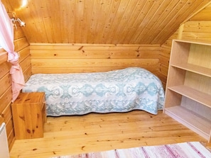 A small wooden room with a bed, a shelf, and a window.