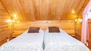 Quarto de cabana de madeira com duas camas, cada uma com travesseiro e edredom estampado.