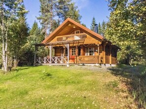 A wooden cabin with a porch, surrounded by trees.