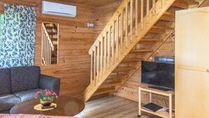 Um interior em madeira com escada, sofá, mesa de centro e uma televisão sobre um suporte.