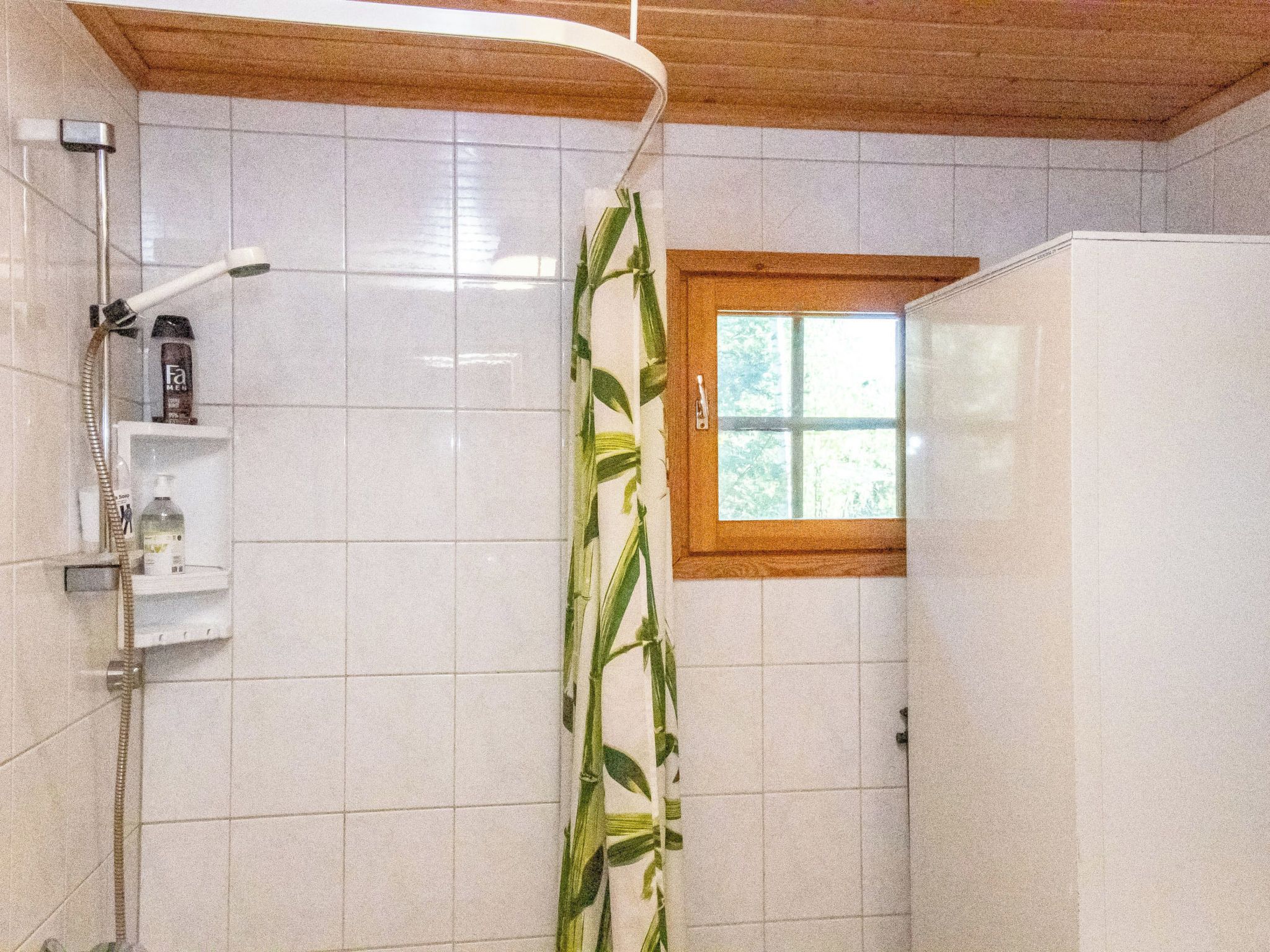 Une salle de bain avec une douche, une fenêtre et une étagère où sont rangés les articles de toilette.