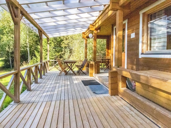 A wooden deck with a glass roof, outdoor furniture, and a view of a forested area.