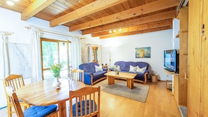 Een woonkamer met houten vloer, een eettafel, blauwe banken en een televisie.