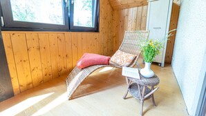Een houten kamer met een rieten stoel, een tafeltje met een vaas en een deur.