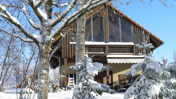 Een houten chalet met balkon, omringd door met sneeuw bedekte bomen.