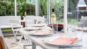 A conservatory with a table set for dining, surrounded by chairs, and a bottle of wine on the table.
