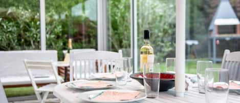 A conservatory with a table set for dining, surrounded by chairs, and a bottle of wine on the table.